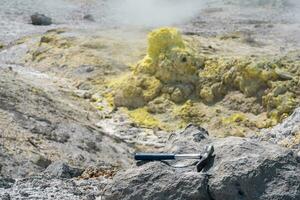 geological hammer on the rock against the backdrop of an steaming fumarole on the slope of a volcano photo