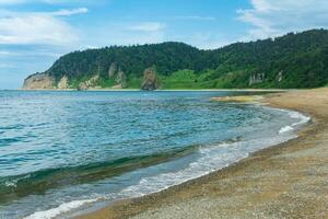 coastal landscape, pebble beach and beautiful wooded rocks on the green coast of Kunashir island photo