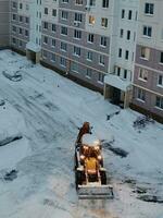 In the morning in the courtyard of a multi-storey building, a yellow tractor clears the snow, selective focus photo