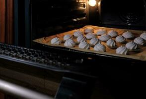 en el cocina, blanco merengues son cocido en un horneando sábana en el horno foto