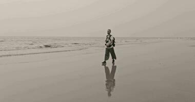 male tourist with a backpack walks along the sandy shore of the sea or ocean at sunset video