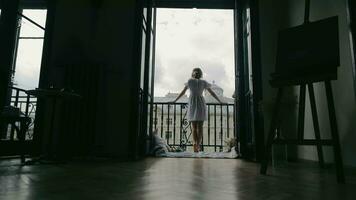 arrière vue de une silhouette de une femme permanent sur une balcon. Matin dans le Hôtel et une nuageux ville journée dans le Contexte. une solitaire femme sur le balcon est en portant le balustrade avec sa mains. video