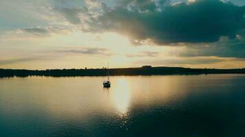 Antenne Aussicht einer Yacht beim Sonnenuntergang in der Nähe von das Lastkahn. Flug beim Sonnenuntergang in der Nähe von das Yacht mit ein Segel. das Sonne ist reflektiert im das Wasser. video