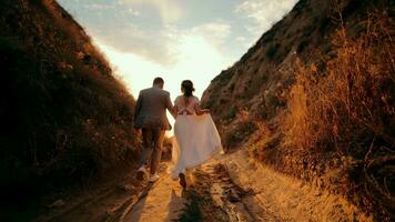 A young couple walks towards the sun between two mountains. Happy people holding hands and walking in front to the sun. Silhouette of a man and a woman on the counter sun. Time together. video