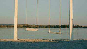 Loneliness and loneliness concept. A lonely teddy bear is riding on a swing. Two swings, on one of them sits a teddy bear against the background of a lake. video