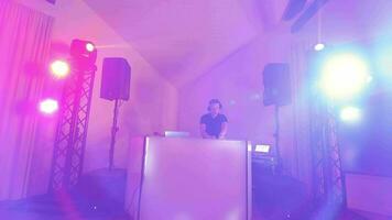 DJ hombre detrás un DJ consola giros música a un fiesta. dinámica cámara movimiento y trabajo de un DJ a un disco. video