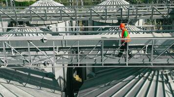 Worker Inspecting Grain Facility, Worker in orange vest on metal walkway inspecting grain storage facility. video