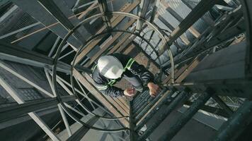 industrieel arbeider beklimming ladders omhoog. top visie, arbeider met moeilijk hoed oplopend de ladder in een industrieel omgeving. video