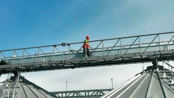 trabajador inspeccionando grano instalaciones desde alto pasarela trabajador caminando en el alto metal pasarela inspeccionando un grano almacenamiento y Procesando instalación. video