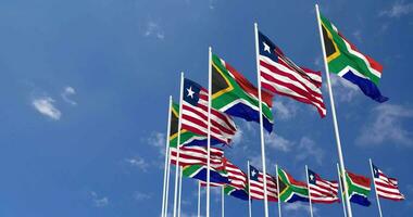 Liberia e Sud Africa bandiere agitando insieme nel il cielo, senza soluzione di continuità ciclo continuo nel vento, spazio su sinistra lato per design o informazione, 3d interpretazione video