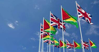 Guyane et uni Royaume drapeaux agitant ensemble dans le ciel, sans couture boucle dans vent, espace sur la gauche côté pour conception ou information, 3d le rendu video