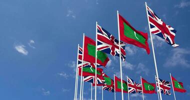 Maldives et uni Royaume drapeaux agitant ensemble dans le ciel, sans couture boucle dans vent, espace sur la gauche côté pour conception ou information, 3d le rendu video