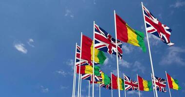 Guinea and United Kingdom Flags Waving Together in the Sky, Seamless Loop in Wind, Space on Left Side for Design or Information, 3D Rendering video