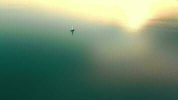 Antenne Aussicht einer Yacht beim Sonnenuntergang im das öffnen Meer. Flug beim Sonnenuntergang in der Nähe von das Yacht mit ein segeln Aussicht von ein Höhe. das Sonne ist reflektiert im das Wasser. video