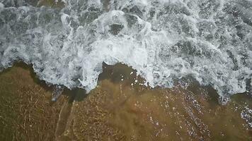 Top view of a sea wave arriving at a sandy beach in slow motion. Sea water foaming from hitting a sandy shore. A tourist's view of the sandy seashore in slow motion video