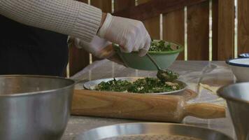 un' uomo nel un grembiule è diffusione pomodoro incolla su un' Pizza Impasto base su un' tavolo cosparso con Farina. su il tavolo nel davanti di lui siamo ciotole di Pizza ingredienti. lui pizzichi il bordi di il Impasto con video