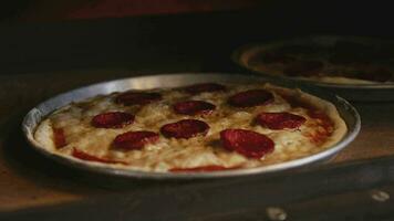 un' uomo nel un grembiule è mettendo crudo Pizza in un' a legna Pizza forno. cucinando cibo al di sopra di un Aperto fuoco. naturale cibo. napoletano Pizza nel il forno. fatiscente formaggio su il superficie di il Pizza. video