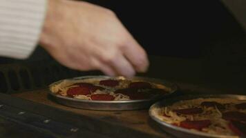 A man in an apron is putting raw pizza into a wood-fired pizza oven. Cooking food over an open fire. Natural food. Neapolitan pizza in the oven. Crumbling cheese on the surface of the pizza. video