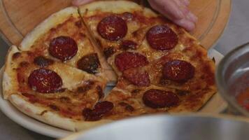 un hombre en un delantal tira Pizza fuera de un a leña horno. un cocinar tira fuera un cocido Pizza. ardiente comida en un a leña horno. grande cuchillo cortes Pizza con queso. Cocinando comida terminado un abierto fuego. natural video