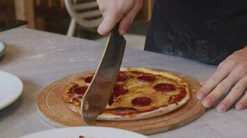 une homme dans un tablier tire Pizza en dehors de une au feu de bois four. une cuisinier tire en dehors une cuit Pizza. brûlant nourriture dans une au feu de bois four. grand couteau coupes Pizza avec fromage. cuisine nourriture plus de un ouvert Feu. Naturel video