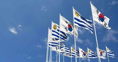 Uruguay e Sud Corea bandiere agitando insieme nel il cielo, senza soluzione di continuità ciclo continuo nel vento, spazio su sinistra lato per design o informazione, 3d interpretazione video