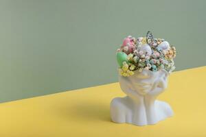 Plaster head statuette with Easter eggs and flowers. Easter creative concept photo