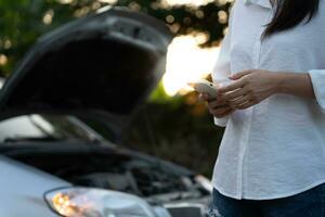 breakdown, broken car, repair. Woman uses mobile phone check insurance premiums through application due to car accident . Find garage to get car fixed during country tour, waiting for help, emergency. photo