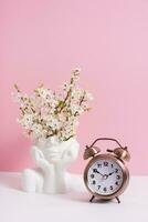 Alarm clock and head shape vase with spring bloom flowers on pink background photo