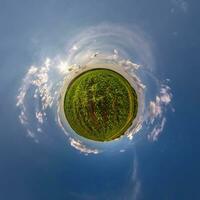 green tiny planet in evening blue sky with beautiful clouds. Transformation of spherical panorama 360 degrees. Spherical abstract aerial view. Curvature of space. photo