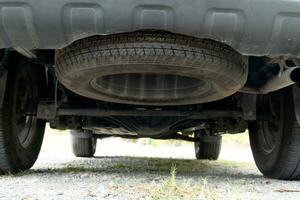 Maintenance background of car's suspension reveals the rear drive shaft. Cars parked on the soil road with gravel. photo