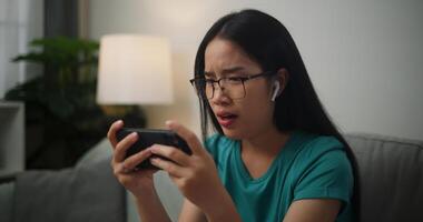 Portrait of Young Asian woman serious playing an online game frustrated with loss or failure sitting on sofa in living room at home.Gamer lifestyle concept photo