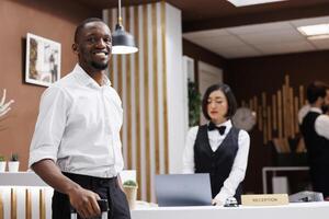 Male tourist sitting at front desk to register and fill in check in forms, guest smiling and waiting for hotel service. Young man standing near reception counter in lobby, luxury resort. photo