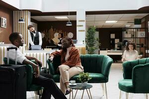 Two hotel guests sitting in lounge area before receptionist helping them with check in process, accommodation. Young couple arriving at luxury resort early, waiting to register. photo