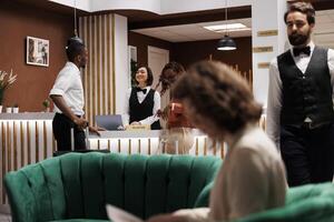 Man welcoming people at front desk, providing excellent service with registration at hotel. Male reception worker talking to guests in lobby, looking to book room at resort upon their arrival. photo