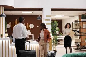 Two people checking in at hotel and taking key card from reception counter, walking to room upon their arrival. Young couple registering at front desk after waiting in resort lobby. photo