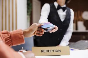 Female tourist paying at pos terminal in hotel lobby, using electronic payment at check in registration. Young resort guest using credit card at reception counter front desk. Close up. photo