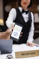 Guest paying with nfc on phone at pos terminal, hotel staff helping tourists with registration forms. Receptionist welcoming people, young man making payment for booking. Close up. photo