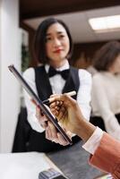 African american woman signing papers to do check in process with receptionist at front desk. Hotel guest filling in registration files at reception, talking to employee about service. Close up. photo