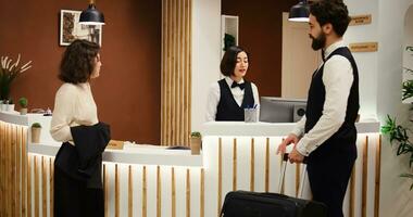 Business travelling woman resort visitor in professional trip assisted by concierge personnel. Tourist doing check in process in posh hotel, being helped by bellboy with luggage photo