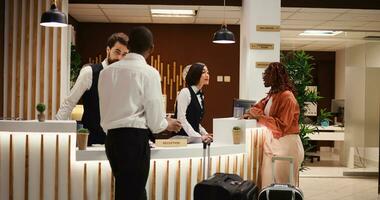 Friendly smiling concierge personnel assisting tourists with room registration. Cheerful front desk receptionists answering customer inquiries about hotel amenities during guests check in process photo