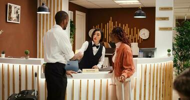Friendly asian receptionist offering room key to happy guests after check in process is finalized. Busy exhausted hotel manager ensuring booking paperwork details are correct photo