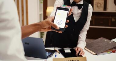 Close up of african american hotel visitor using smartphone banking app to buy holiday package deal upgrade. Receptionist using POS payment terminal to validate credit card purchase during check in photo