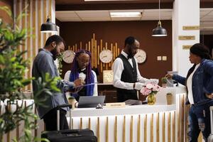 Young African American couple filling up registration form while checking in at hotel front desk. Tourists arriving at resort signing documents during check-in procedure, standing at reception area photo