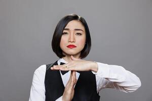 Restaurant serious asian waitress dressed in uniform showing timeout symbol with palms portrait. Catering service woman worker making interruption gesture and looking at camera photo