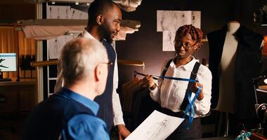 Client working with luxury couturier to create custom made tailored suit, customer talking to tailor and assistant about body measurements. Employee using measuring tape in atelier. photo