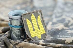 Ukrainian army symbol and bunch of dollar bills on military uniform. Payments to soldiers of the Ukrainian army from United States, salaries to the military. War support photo