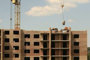 View of a large construction site with buildings under construction and multi-storey residential homes. Tower cranes in action on blue sky background. Housing renovation concept photo