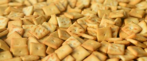 A lot of small cookies are square shaped. A pattern of a yellow salt cracker. Background image with salted pastry photo