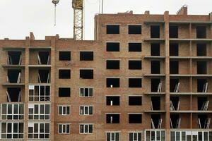 View of a large construction site with buildings under construction and multi-storey residential homes. Tower cranes in action on blue sky background. Housing renovation concept photo