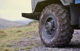 Wheel closeup in a countryside landscape with a mud road. Off-road 4x4 suv automobile with ditry body after drive in muddy road photo